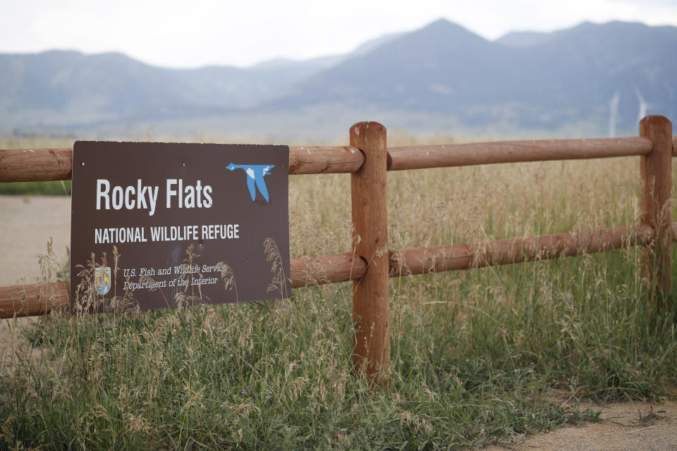 In this Wednesday, Aug. 7, 2019 photo, a sign hangs from a fence at the head of a trail at the Rocky Flats Wildlife Refuge in Arvada, Colo. The U.S. Energy Department manufactured plutonium triggers for nuclear warheads at Rocky Flats. It had a long history of leaks, fires and environmental violations. Its rare tallgrass prairie is home to hundreds of species, including an endangered jumping mouse. Part of the site is open to the public. (AP Photo/David Zalubowski)