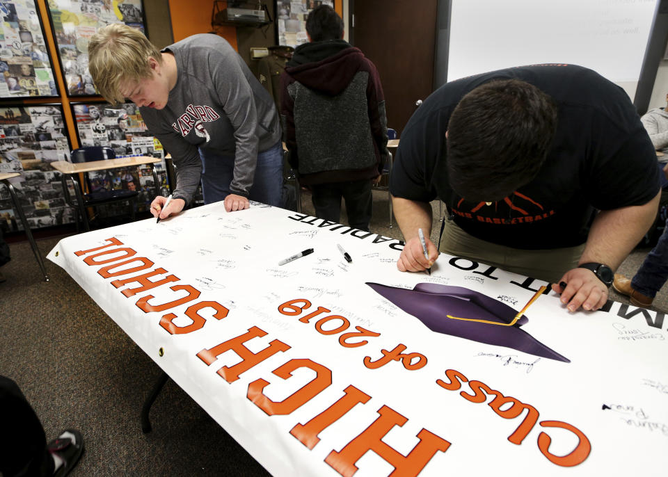 Braxton Moral, 16, left, signs the Class of 2019 "Commitment to Graduate" banner after hearing a speech from Principal Mark Paul at Ulysses High School in Ulysses, Kan., on Wednesday, Dec. 12, 2018. (Sandra J. Milburn/The Hutchinson News via AP)