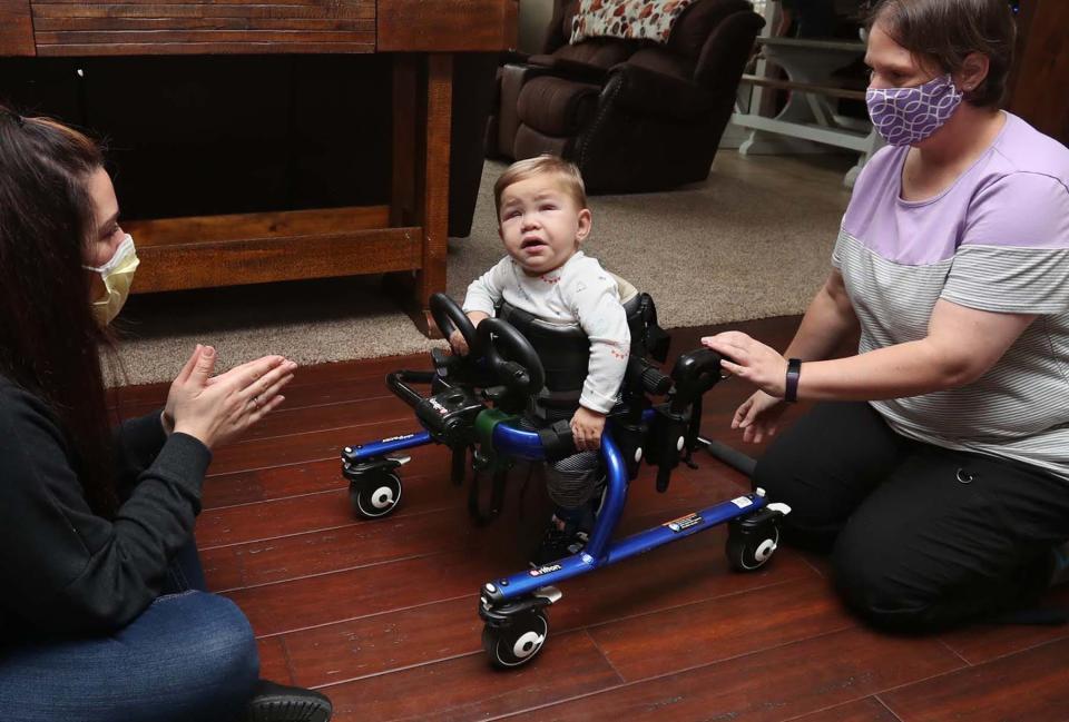 Carlla Detwiler, left, cheers on 19-month-old David Detwiler to take a step during a session with physical therapist Jenn Masser in Massillon.