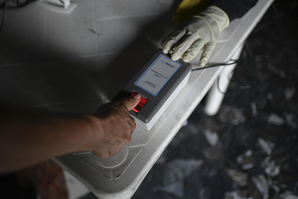 A woman places her thumb on a handheld fingerprint scanner at a validation center to certify the authenticity of voter data in Caracas, Venezuela, Saturday, July 25, 2020, amid the new coronavirus pandemic. The legislative election is scheduled for Dec. 6 and thus far the opposition has indicated it will not participate. (AP Photo/Matias Delacroix)