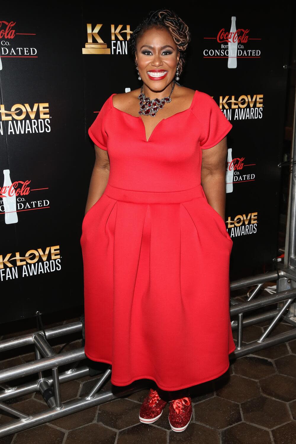 Mandisa smiling with her hands in the pocket of a tea-length short-sleeve red dress