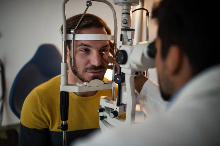 A man receives an eye exam from an optometrist using specialized equipment. Both are focused on the procedure. 