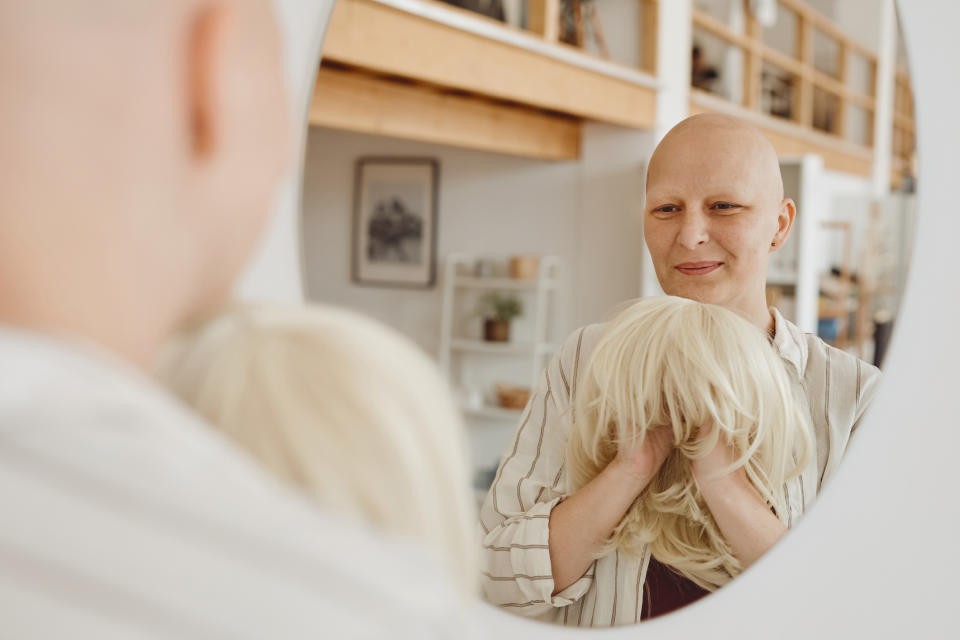 A bald patient holding up a blonde wig and smiling