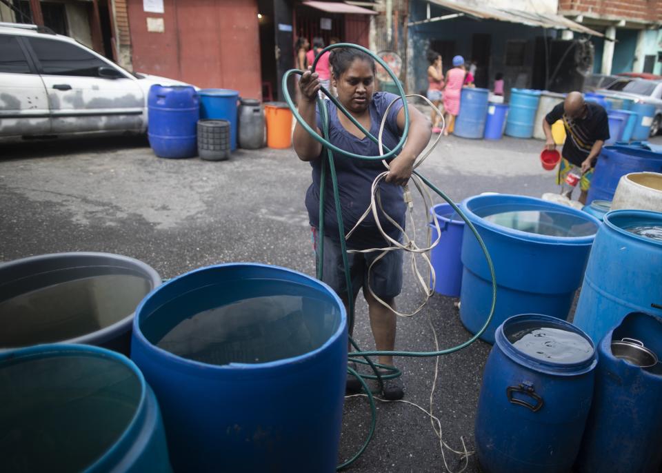 A woman untangles an electrical cord and a hose in order to pump from a large container water provided by a government tanker truck, in the Petare slum of Caracas, Venezuela, Wednesday, June 10, 2020. Venezuela's water crisis is nothing new, but water today is even more important due to the new coronavirus pandemic. (AP Photo/Ariana Cubillos)