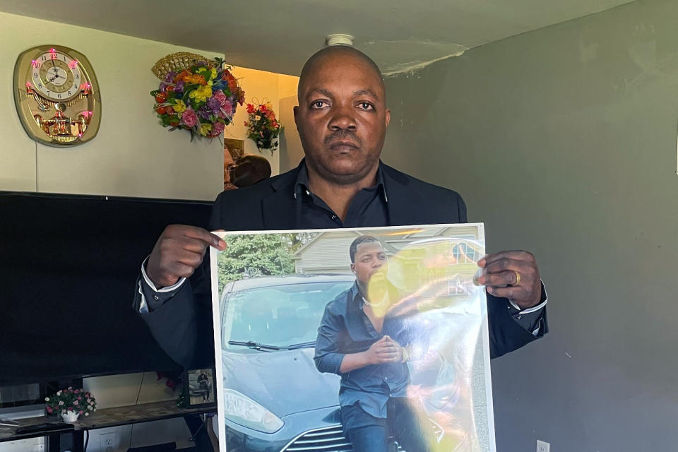Peter Lyoya holds up a picture of his son Patrick Lyoya, 26, in his home in Lansing, Mich., April 14, 2022. Patrick was face-down on the ground when he was fatally shot in the head by a Grand Rapids Police officer after resisting arrest on April 4, 2022. Grand Rapids police released four videos from different sources Wednesday, nine days after Patrick Lyoya was killed during a traffic stop. Prominent civil rights attorney Ben Crump and Lyoya's family are planning to hold a news conference Thursday afternoon. (AP Photo/Anna Nichols)