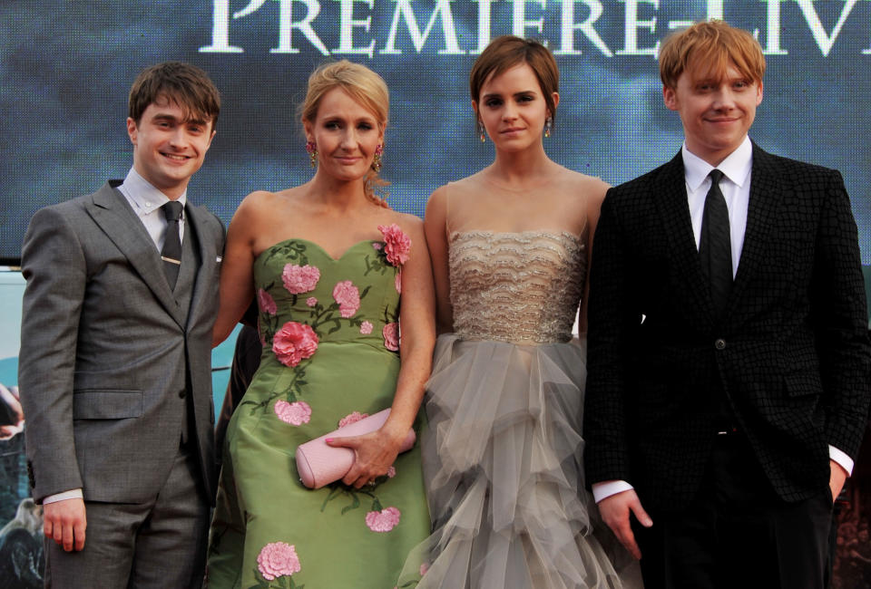 Daniel Radcliffe, J.K. Rowling, Emma Watson, and Rupert Grint posing together at an event. Rowling in a floral dress; others in formal wear