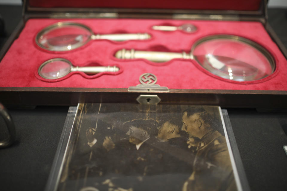 A photo of Nazi leader Adolf Hitler holding a magnifying glass is displayed during a press conference in Buenos Aires, Argentina, Wednesday, Oct. 2, 2019. According to Argentine authorities, they believe that one of the magnifying glasses in the case displayed above the photo is the same one seen in the photo. Both objects are part of a cache of Nazi artifacts seized by the police in 2017. (AP Photo/Natacha Pisarenko)