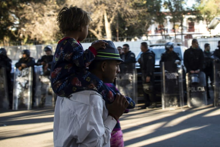 A Central American migrant seeking to reach the United States, while holding a child, walks next to a line of police officers outside of a temporary shelter in Tijuana, Mexico near the US border on November 26, 2018