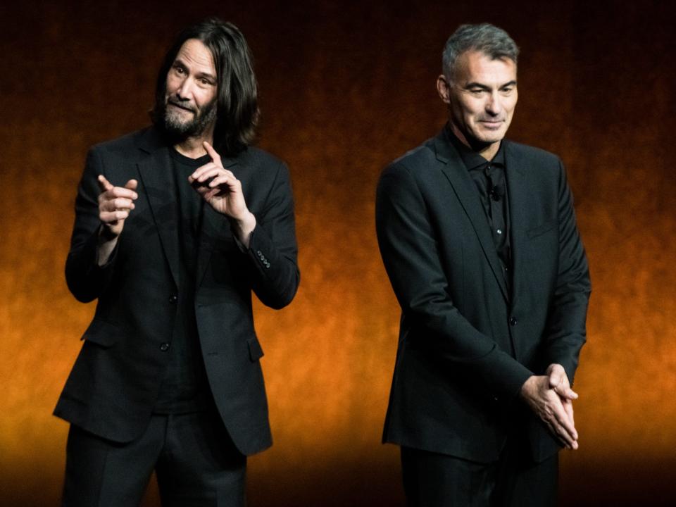 Keanu Reeves and Chad Stahelski smile onstage together while presenting a film at CinemaCon.