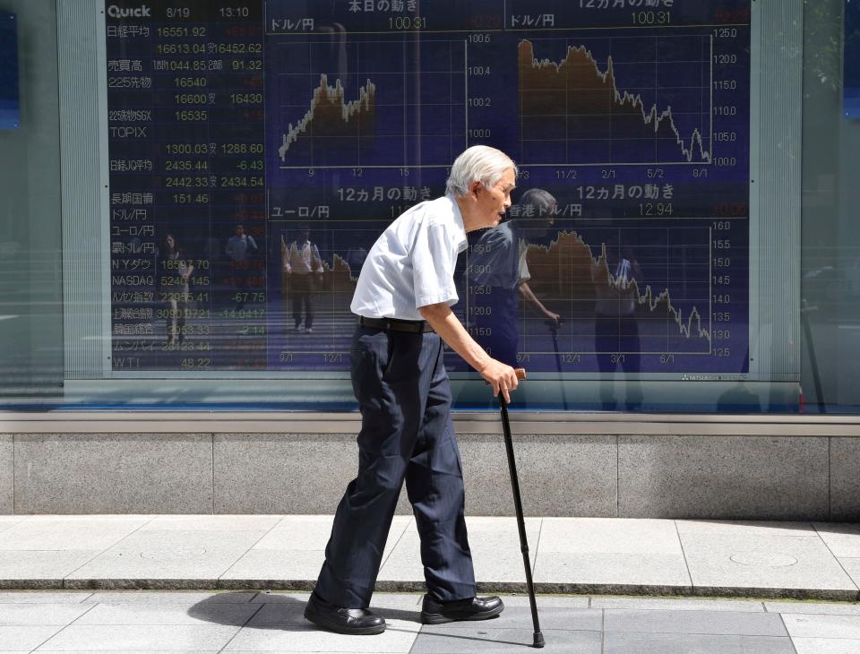 An elderly man walks by an electronic stock board of a securities firm in Tokyo, Friday, Aug. 19, 2016.