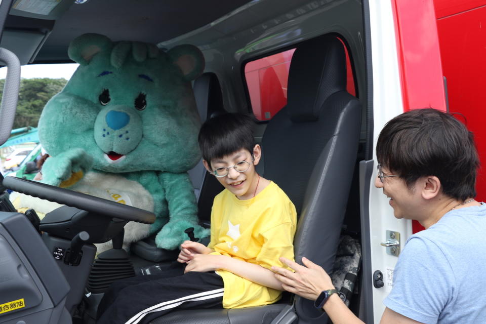 小樂在喜願熊的陪伴下 坐上消防車 右為小樂的父親。   圖：新北市社會局提供