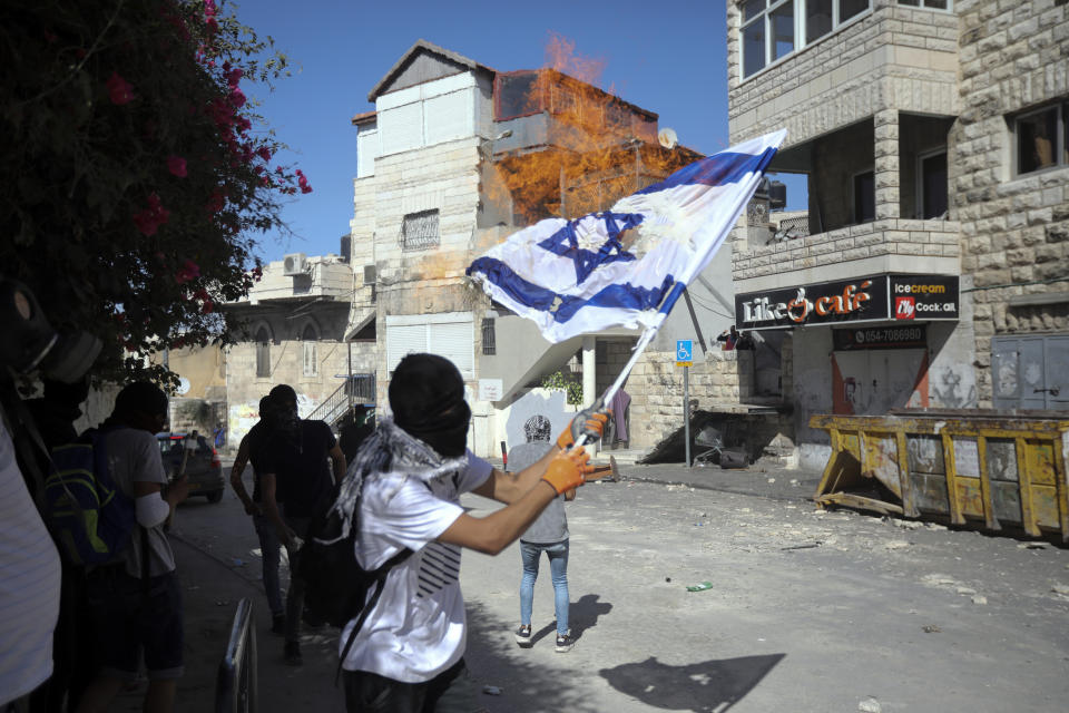 FILE - In this June 28, 2019 file photo, Palestinians burn an Israeli flag during clashes with Israeli police in East Jerusalem's Palestinian neighborhood of Issawiya, a day after a Palestinian was shot and killed by police during a protest in the same neighborhood. Nearly every day for the last nine months Israeli police have stormed into Issawiya in a campaign they say is needed to maintain law and order. Rights groups say that in addition to searching houses and issuing fines, they have detained hundreds of people — some as young as 10, on suspicion of stone-throwing. The operations frequently ignite clashes, with local youths throwing rocks and firebombs. Residents and human rights groups say the provocative raids have created an atmosphere of terror, with parents afraid to let their children play outside. (AP Photo/Mahmoud Illean)