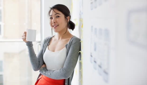 Smiling businesswoman leaning against whiteboard and drinking coffee