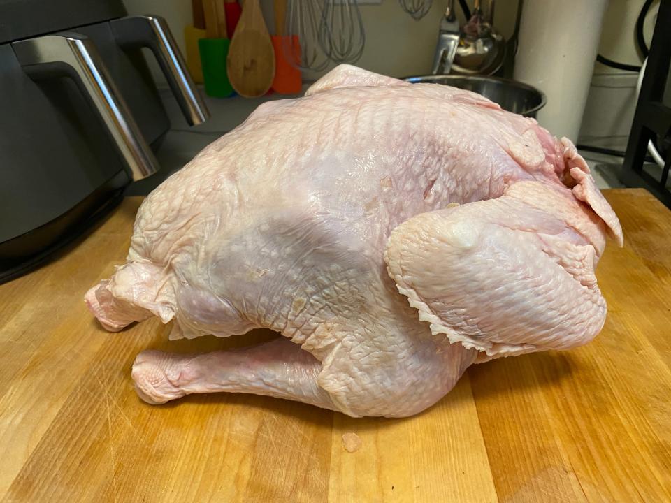 An uncooked turkey on a wooden cutting board.