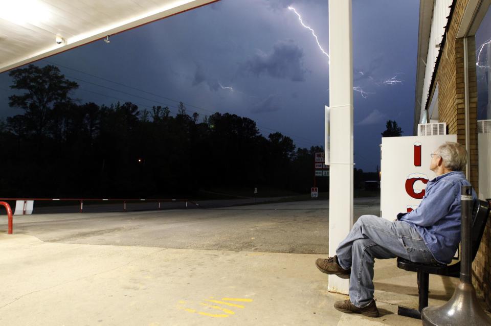 Jimmy Sullinger sits underneath an awning as he watches lightning from a storm approaching the gas station where he works on Monday, April 28, 2014, in Berry, Ala. A dangerous storm system that spawned a chain of deadly tornadoes killed dozens from the Midwest to the Deep South. (AP Photo/Butch Dill)