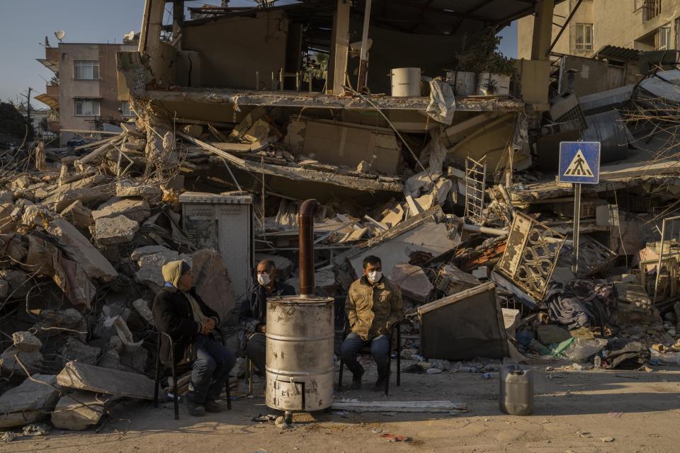 People sit next to a destroyed house as they wait for the bodies of friends and family members to be pulled from the rubble after an earthquake in Antakya, southeastern Turkey, Monday, February 13, 2023. Thousands left homeless by a massive earthquake that struck Turkey and Syria a week ago packed into crowded tents or lined up in the streets Monday for hot meals as the desperate search for survivors entered what was likely its last hours. (AP Photo/Bernat Armangue)