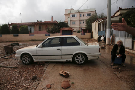 Local Konstantina Louka sits next to a car drifted along by a heavy rainfall in the town of Mandra, Greece, November 15, 2017. REUTERS/Alkis Konstantinidis