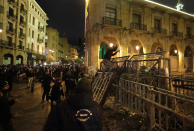 An anti-government protester, center top, stands on barriers defense as he throws stones against the riot police, during ongoing protests against the political elites who have ruled the country for decades, in Beirut, Lebanon, Sunday, Jan. 19, 2020. Lebanese security forces used tear gas, water cannons and rubber bullets in clashes with hundreds of anti-government protesters outside the country's Parliament on Sunday, as violence continued to escalate in a week of rioting in the capital. (AP Photo/Hassan Ammar)