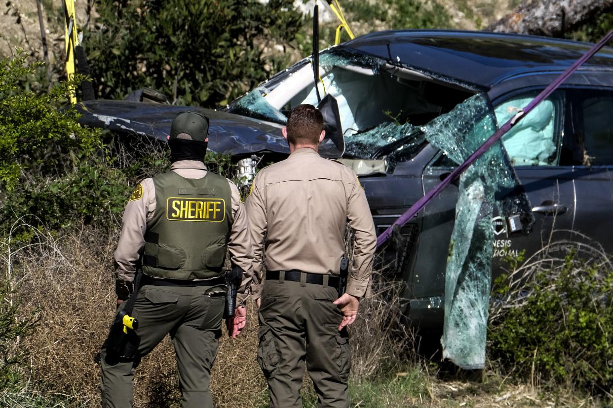 Law enforcement officers watch as a crane is used to lift a vehicle following a rollover accident involving golfer Tiger Woods, Tuesday, Feb. 23, 2021, in the Rancho Palos Verdes section of Los Angeles.