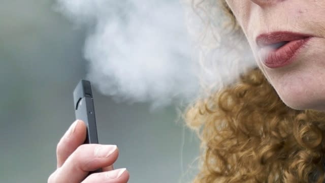 Woman exhales while vaping from a Juul pen e-cigarette.