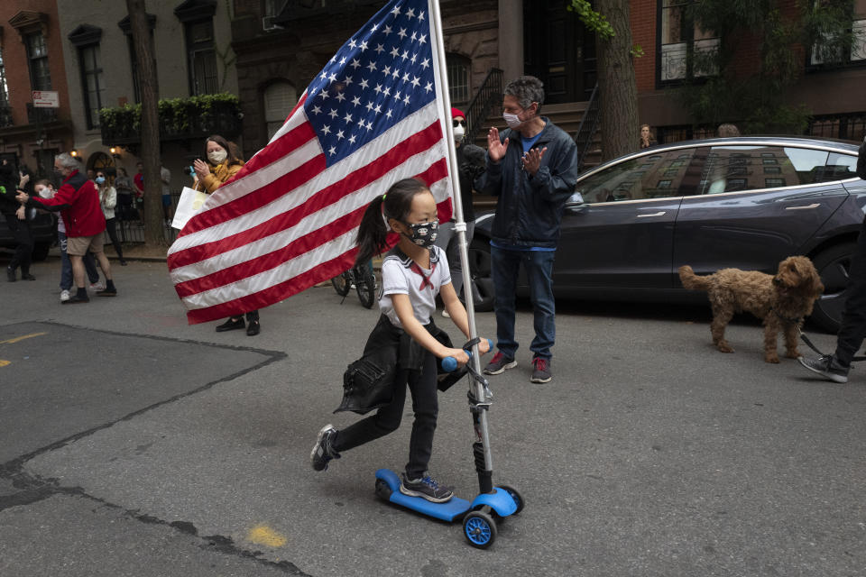 Ai Feng, 6, parades up and down her block with a United States flag in the Greenwich Village neighborhood of New York Thursday, May 14, 2020, during the coronavirus pandemic. The New York City immortalized in song and scene has been swapped out for the last few months with the virus version. In all the unknowing of what the future holds, there’s faith in that other quintessential facet of New York City: that the city will adapt. (AP Photo/Mark Lennihan)