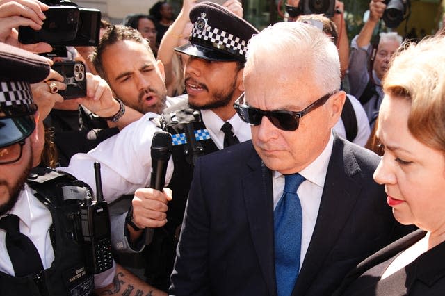 Huw Edwards in dark glasses surrounded by people and police officers