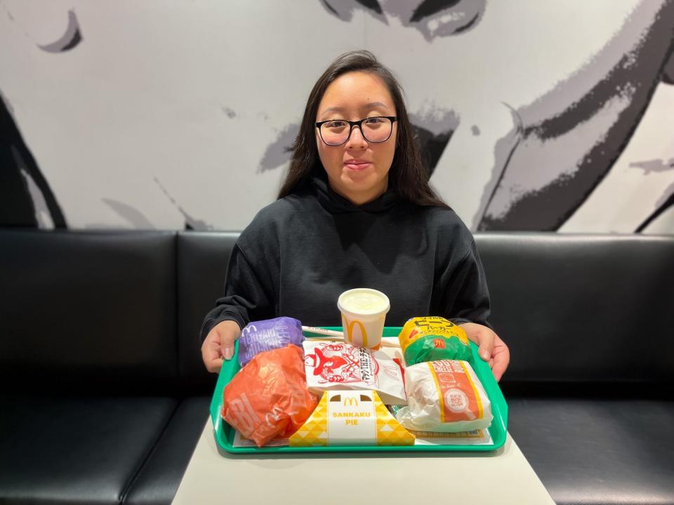 A woman with glasses sits at a table with a tray full of food from McDonald's.