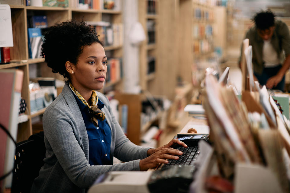 Woman working on a computer in a library with another person in the background