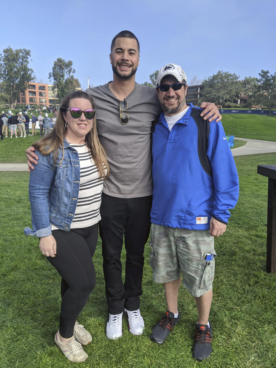 In this photo provided by Lora Greco, Lora and Matt Greco flank then-San Diego Padres baseball player Joey Lucchesi at the 2020 Farmers Insurance Open golf tournament in San Diego. Lora and Matt Greco hosted players in Lake Elsinore — a Class A affiliate for the San Diego Padres — for three seasons from 2017-19. Their tenants included future big-league pitchers Joey Lucchesi and David Bednar. The Grecos said Lucchesi used to stop at a gas station on his way home from games, pick up a movie from a Redbox in the parking lot, and then come home for a family movie night. (Photo Courtesy Lora Greco via AP)