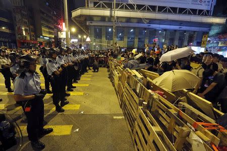 Riot police line up in front of protesters behind a barricade in the Mongkok shopping district of Hong Kong early October 19, 2014. REUTERS/Bobby Yip
