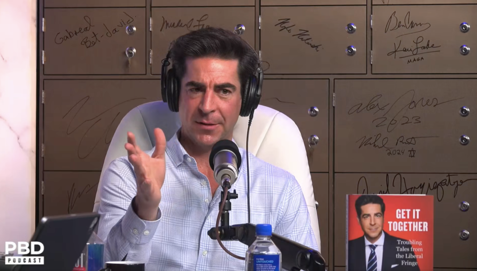 A man gestures while hosting a podcast, with a signed backdrop and his book displayed