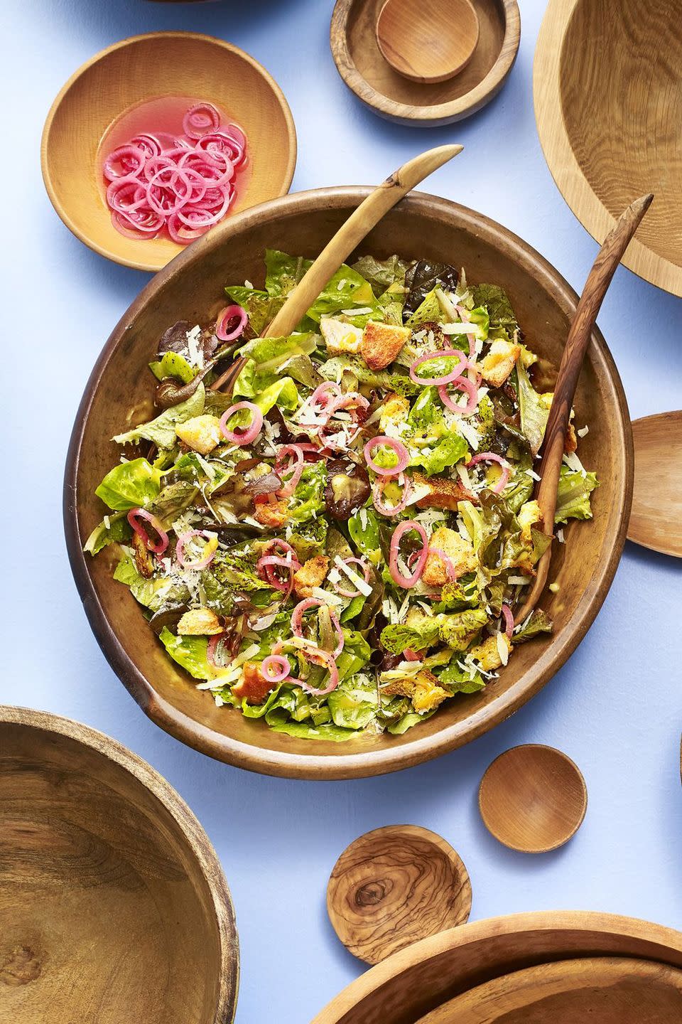 spring greens caesar salad with pickled shallot in a large wooden serving bowl with wooden serving utensils