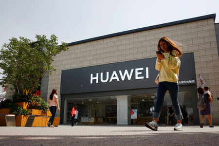 A woman looks at her phone as she walks past a Huawei shop in Beijing, China May 16, 2019. REUTERS/Thomas Peter/Files