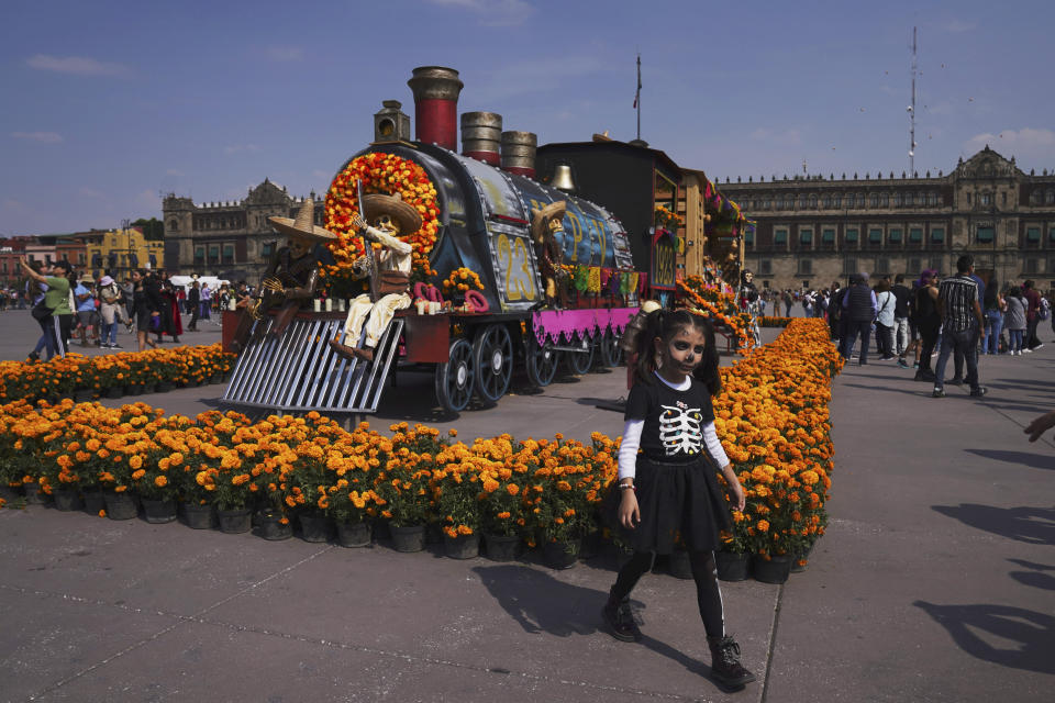 People pose for photos next to a Day of the Dead-themed presentation at Mexico City´s main square the Zocalo, on Tuesday, Oct. 31, 2023. (AP Photo/Marco Ugarte)