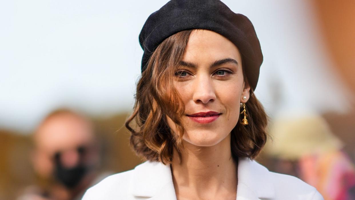 Alexa Chung wears a black wool beret a white long blazer jacket, outside the Dior show