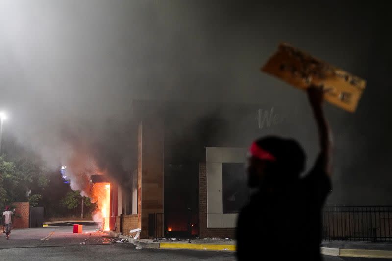 A man holds up a sign in front of a burning Wendy’s following a rally against racial inequality and the police shooting death of Rayshard Brooks, in Atlanta