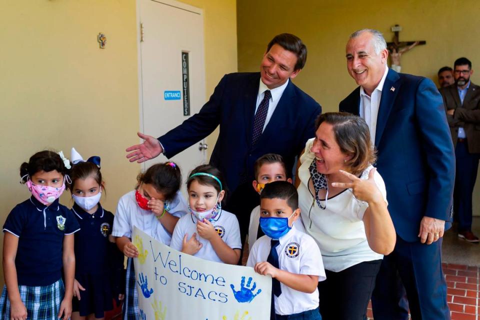 El gobernador Ron DeSantis, a la izquierda, y el ex comisionado del Condado Miami-Dade Esteban Bovo, se toman una foto con estudiantes de St. John the Apostle Catholic School en Hialeah, Florida, el martes 11 de mayo de 2021. DeSantis firmó el martes un proyecto de ley que amplía y moderniza los programas de becas y cupones escolares de la Florida.