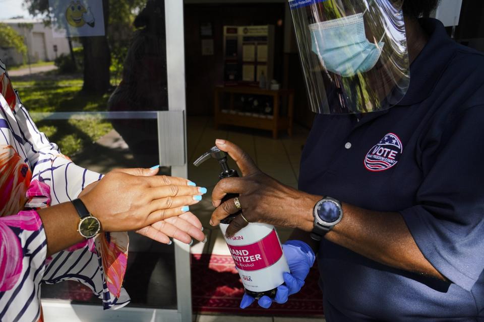 Pinellas School Board member, Rene Flowers, who is running for Pinellas County Commission District 7, arrives at Galilee Missionary Baptist Church to cast her ballot, on voting day. Poll worker, Gloria Nelson, 67, of St. Petersburg, provides Flowers with hand sanitizer before entering the polling station. Tuesday, Aug. 18, 2020 in St. Petersburg. (Martha Asencio Rhine/Tampa Bay Times via AP)