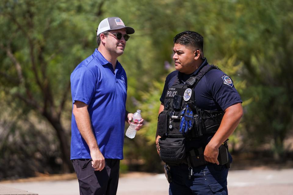 Tyler Bowyer, chief operating officer of Turning Point Actions, left, speaks with a Mesa police officer regarding photojournalists from the Arizona Republic photographing a get out the vote rally event put on by Turning Point Action on Saturday, July 30, 2022, in Mesa. Bowyer threatened to call the police after accusing journalists of harassment for photographing the event, which was held in a public park.