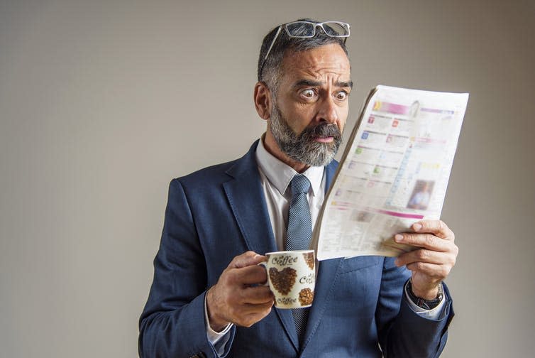 Man looking shocked reading the newspaper.