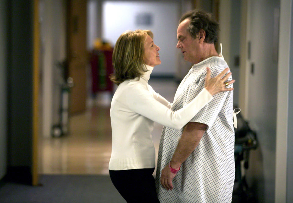 Two characters, a woman in a white shirt and a man in a hospital gown, appearing to console each other in a corridor