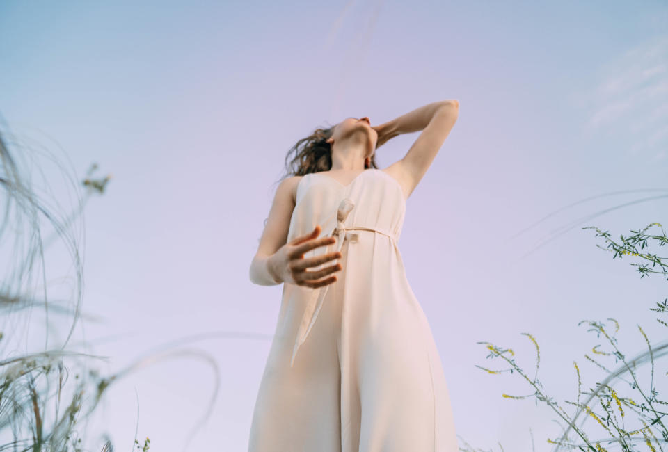 Frau in leichtem Kleid vor pastellblauem Himmel.