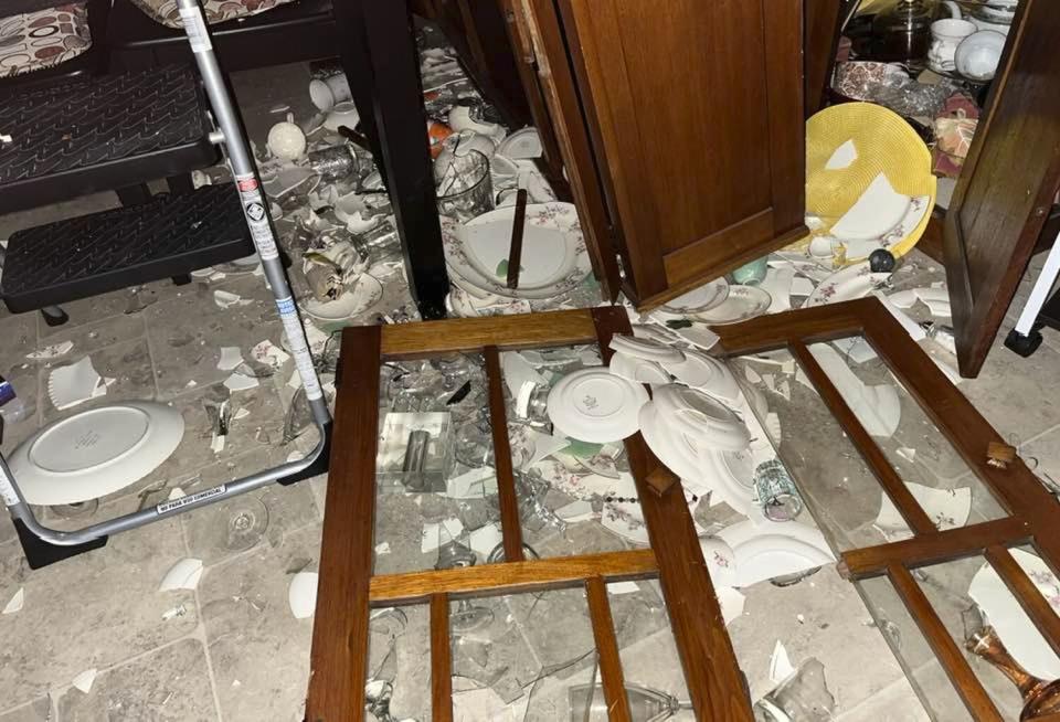 A horizontal view of a kitchen floor with broken dining ware and cupboard doors.