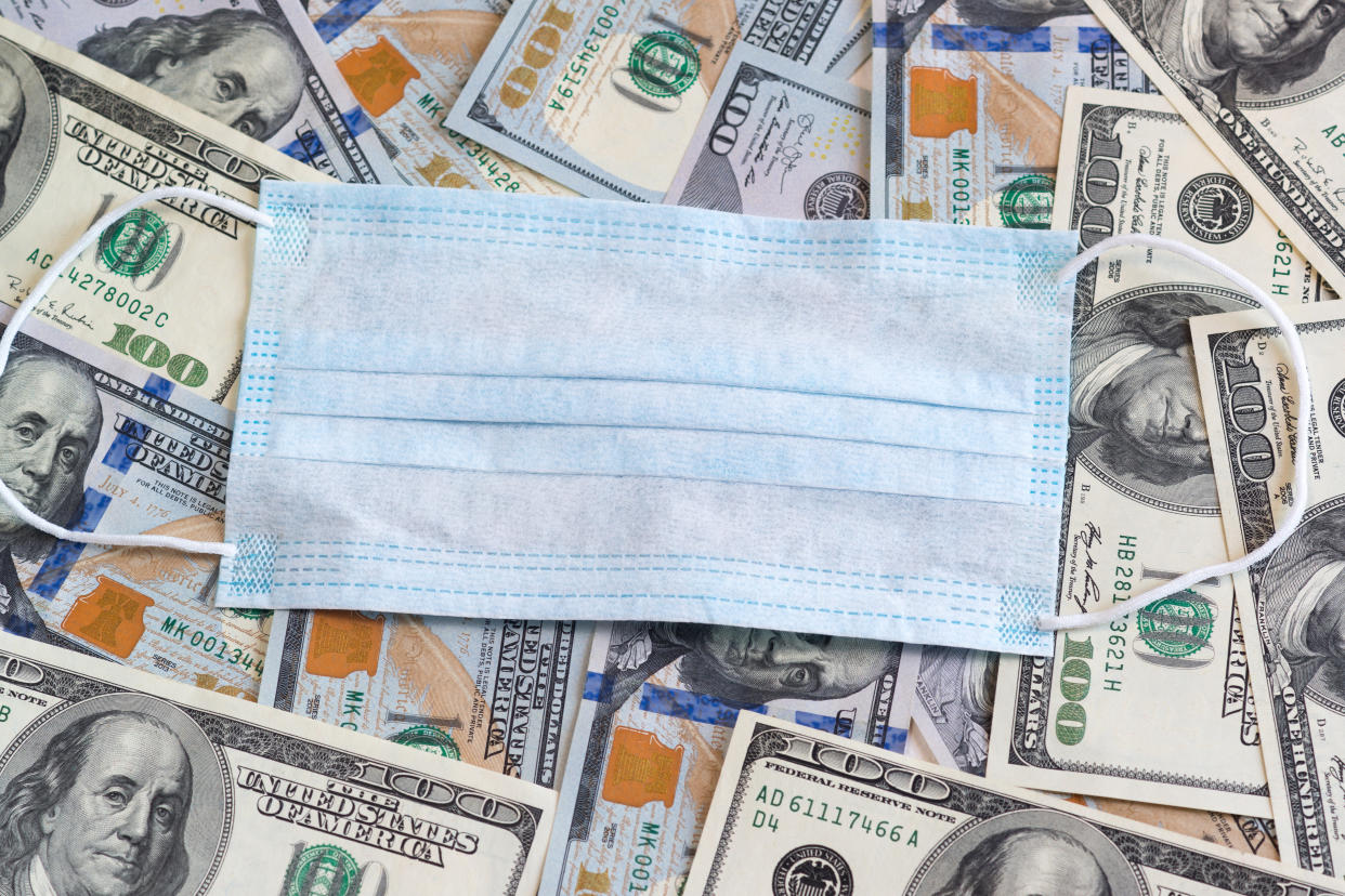 The disposable medical mask is on top of the hundred-dollar bills. Protecting businesses during the covid-19 coronavirus epidemic. Damages