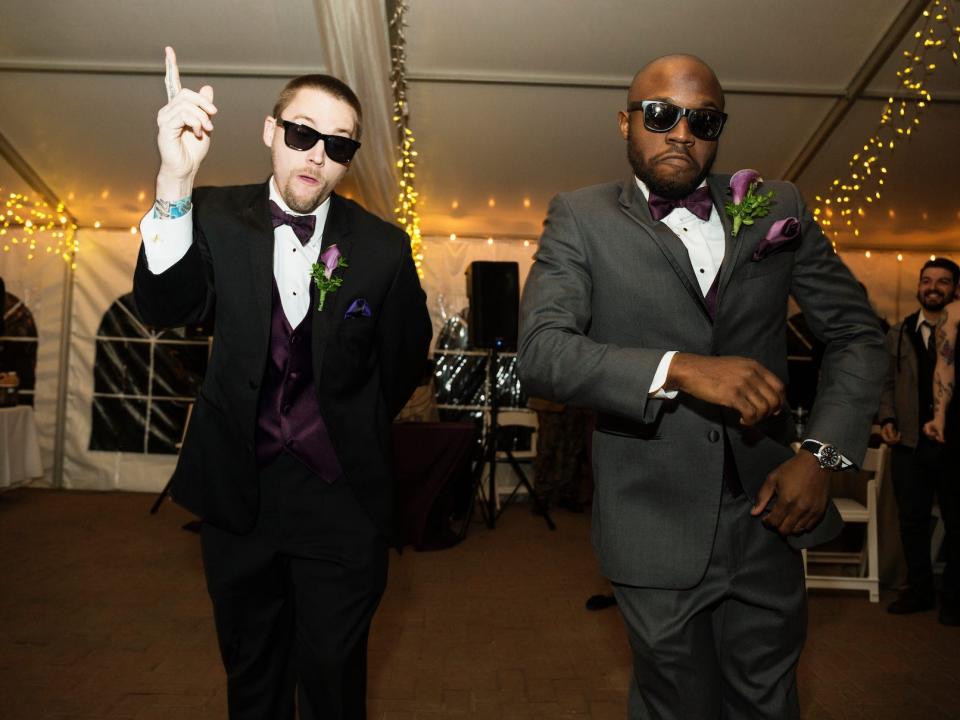 A groom and a groomsman dance in tuxedos at a wedding.