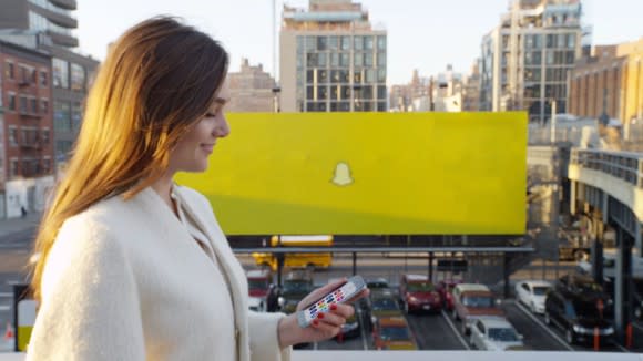 Snapchat app user smiling at a phone, with a Snapchat billboard in the background