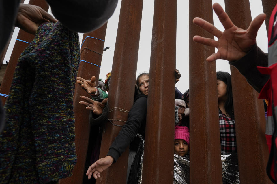 Migrants reach through a border wall for clothing handed out by volunteers as they wait between two border walls to apply for asylum Friday, May 12, 2023, in San Diego. Hundreds of migrants remain waiting between the two walls, many for days. The image was part of a series by Associated Press photographers Ivan Valencia, Eduardo Verdugo, Felix Marquez, Marco Ugarte Fernando Llano, Eric Gay, Gregory Bull and Christian Chavez that won the 2024 Pulitzer Prize for feature photography. (AP Photo/Gregory Bull)