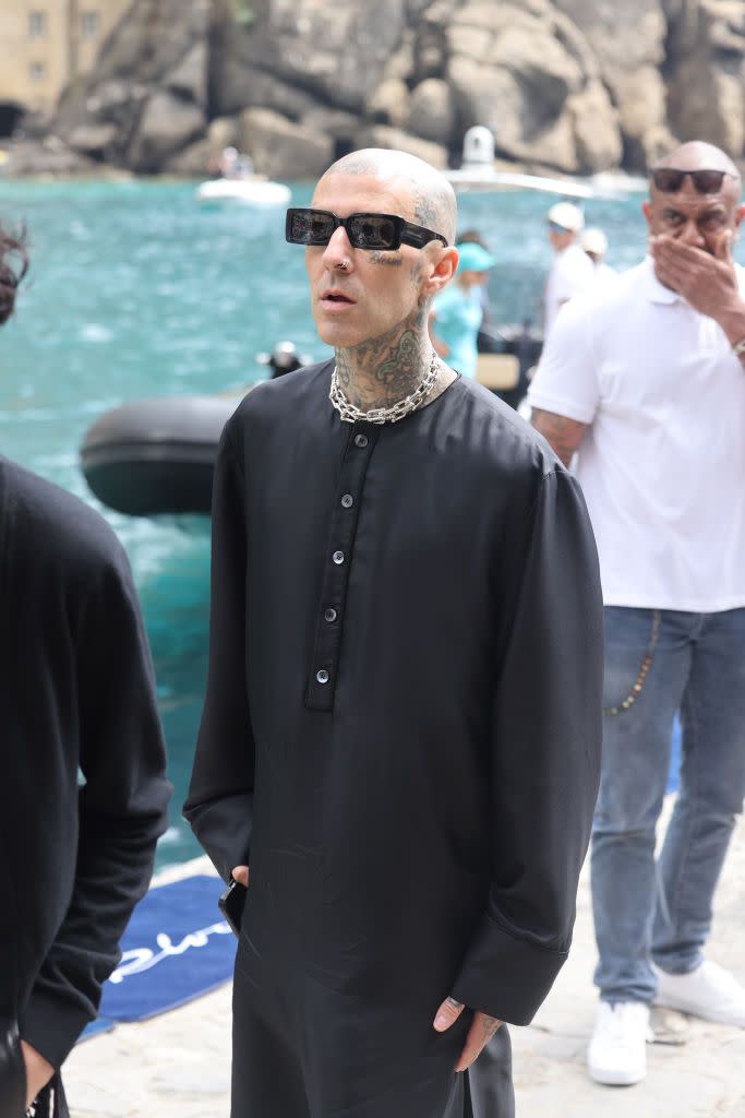 <p>Travis keeps it simple with a long black tunic with button detailing, chain necklace and Y2K sunglasses. </p>