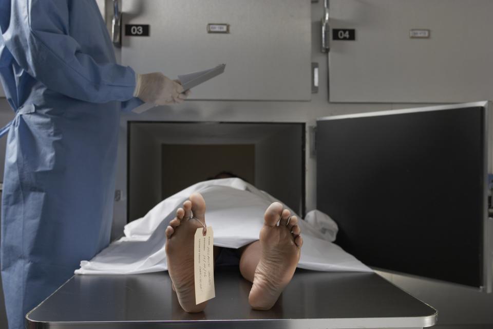 Un médico forense toma notas frente a un cadáver en una morgue