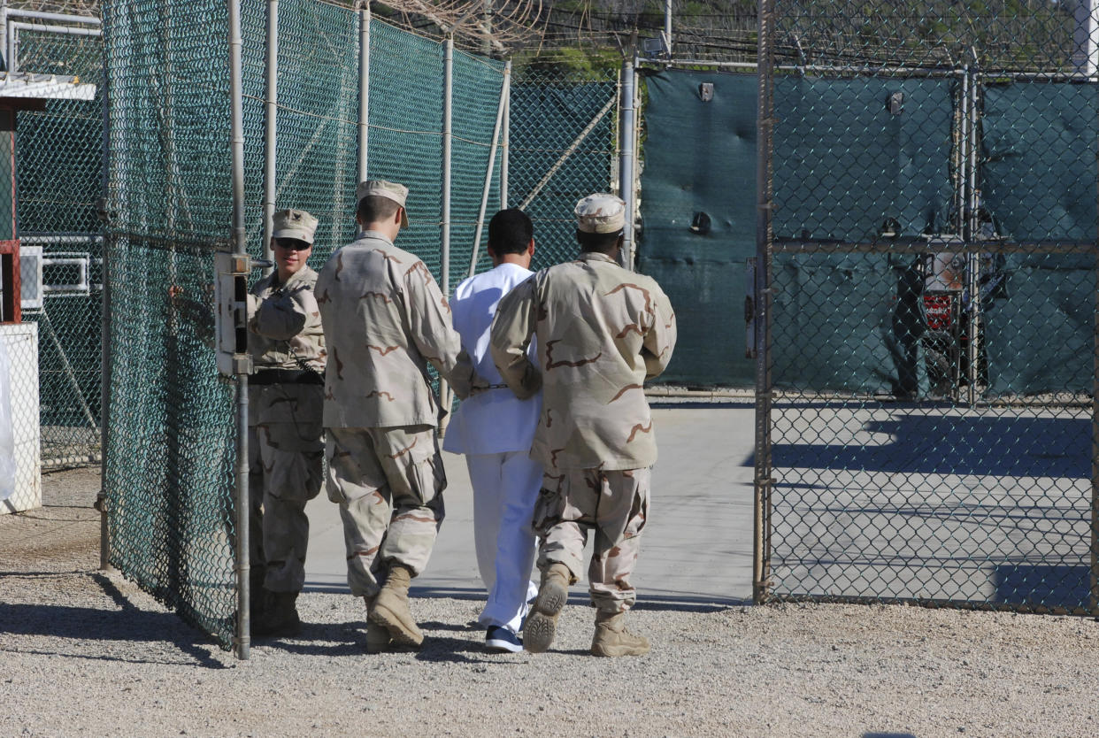 Two U.S. Navy guards flank a detainee as they escort him across the facility at Guantánamo Bay.